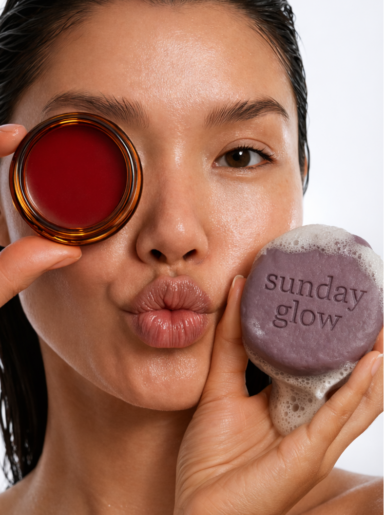 Woman holding a bottle of red liquid and a purple scrub with 'sunday glow' branding.