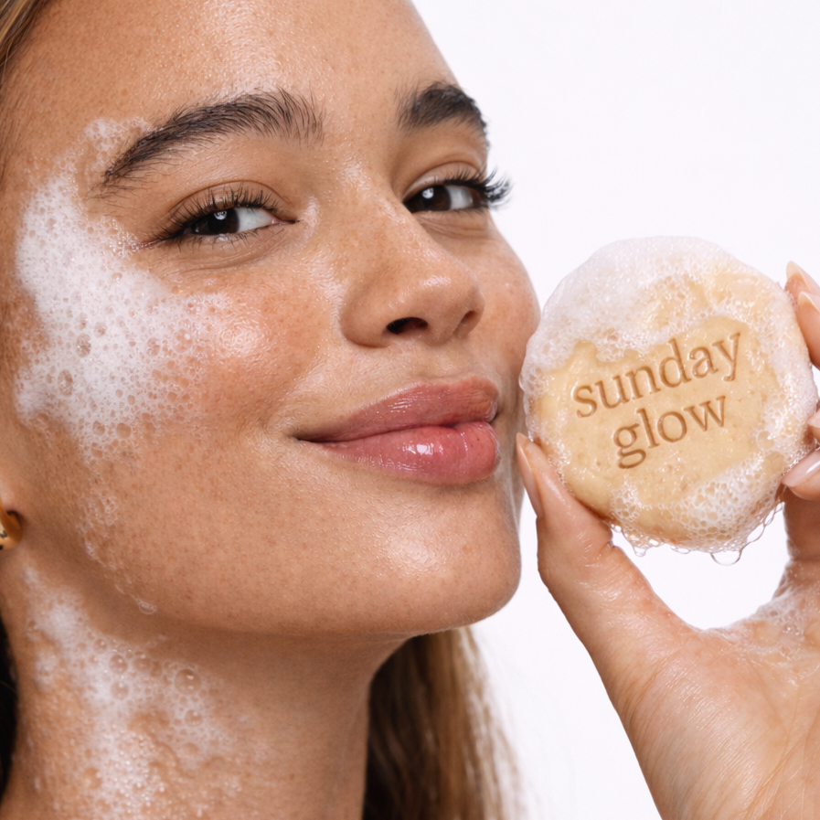 Woman applying foamy cleanser to her face with a 'sunday glow' bar of soap.