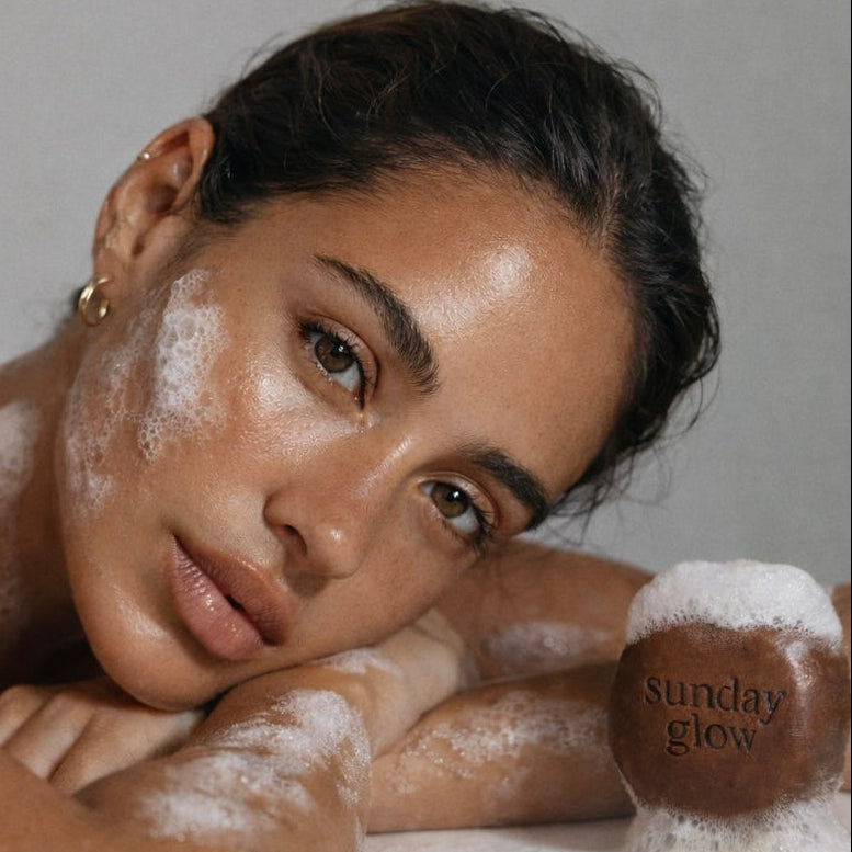Woman with a sun-kissed glow holding a 'Sunday Glow' product against a neutral background